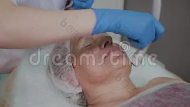 专业美容师在美容办公室为一名携带微电流的老年妇女执行手术。